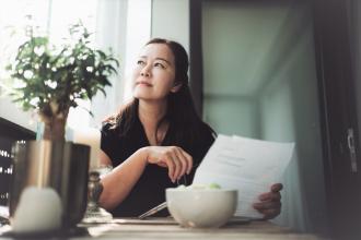 Asian woman thinking while reading and working on her laptop