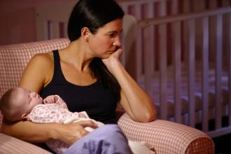 Depressed mother holding her baby sitting in a armchair 