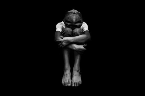 A young boy sits by himself with his arms wrapped around his knees