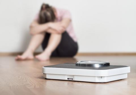 A woman sits beside a scale, with her head in her hands
