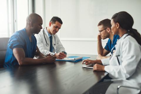 A group of doctors is sitting around a boardroom table and talking