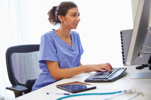 A doctor sits at a computer, typing on the keyboard
