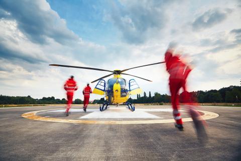 Three people in red suits are running to an air rescue helicopter