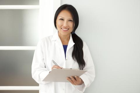 A doctor stands in a hallway, writing on a clipboard