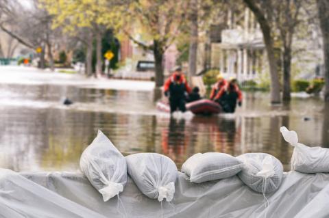 Rescuers traverse a flooded street by boat; sandbags are seen in the foreground
