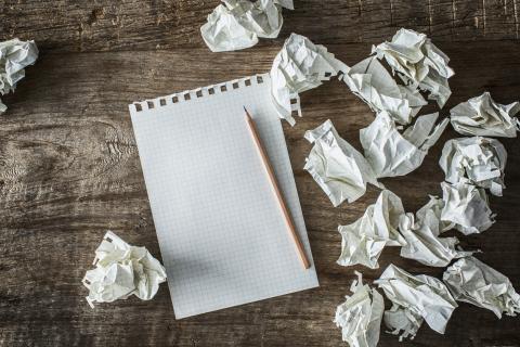 Crumpled sheets of paper beside a notebook and pencil