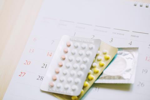 Birth control pills and a condom on top of a calendar