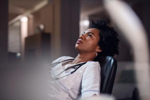 A tired doctor sits at her desk, leaning back in her chair