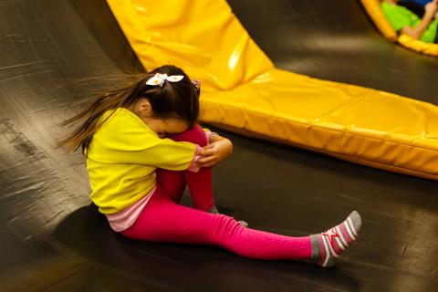 A young girl sits on a trampoline, holding her knee.
