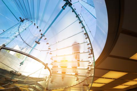A view from underneath of two people walking down a circular glass staircase.