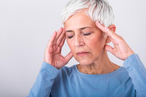 A woman presses her hands to the sides of her head, looking confused and in pain