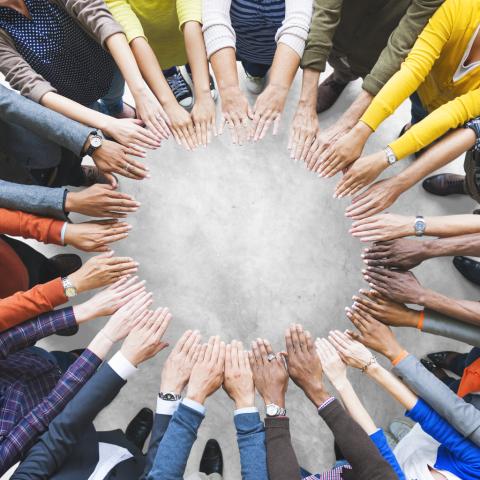 A group of people stand in a circle, with their hands in the centre