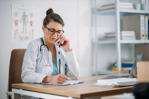 A doctor takes notes while talking on the phone
