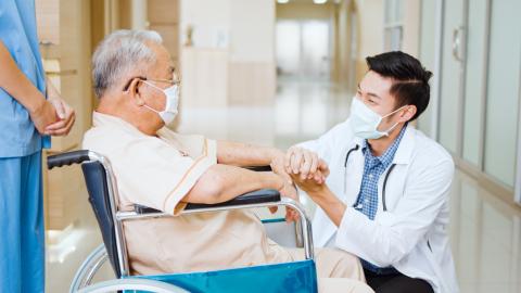 A doctor crouches down to talk to a senior in a wheelchair