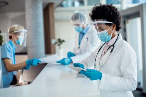 Doctors and nurses doing paperwork at a nursing station while wearing masks and face shields