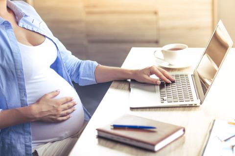 A pregnant woman works on a computer