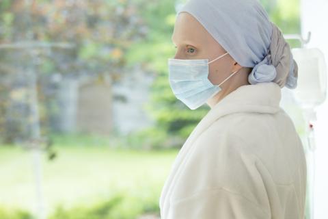 A cancer patient wearing a face mask looks out the window from a hospital room