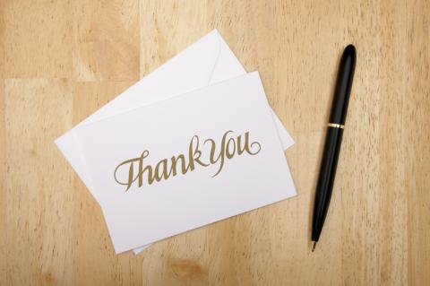 A note card with the words "Thank you" sits on a desk, with a pen beside it