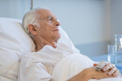 A senior reclines in a hospital bed, breathing from an oxygen mask