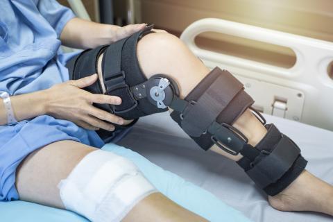 A patient sits on a hospital bed with a knee brace on