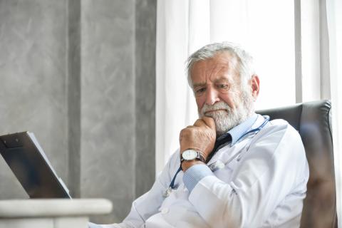 A doctor sits at a desk, looking thoughtful