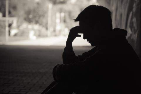 A man sits on the floor in a hallway in shadows