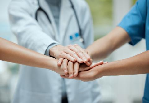 A group of health care professionals stand in a circle with their hands stacked on top of each other