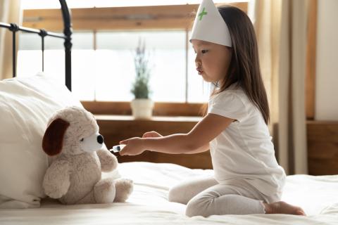 A child dressed up as a doctor pretends to give a vaccine to a stuffed animal