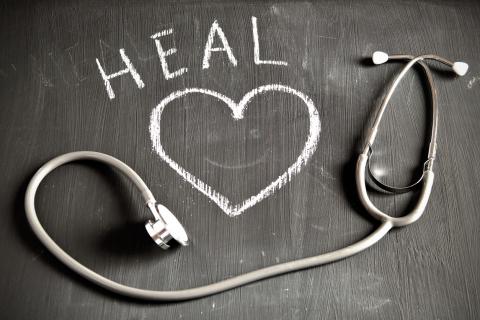 A stethoscope sits on a chalk board with a heart and the word "HEAL" written on it