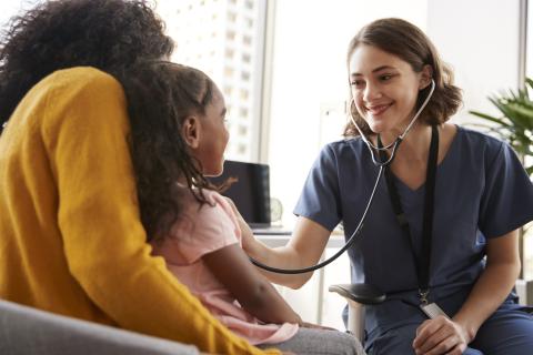 A doctor talks to a child and their parent while using a stethoscope on the child