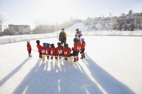 Two coaches stand talking to a kids' hockey team