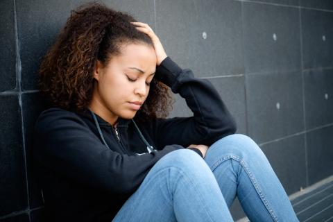 A youth sits in a hallway, leaning against the wall and looking upset