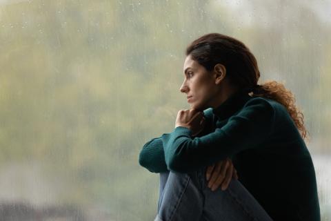 A woman sits by the window looking sad