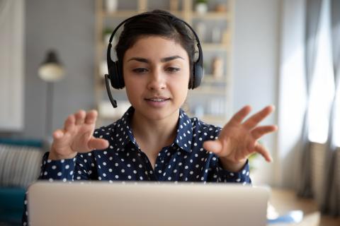 An interpreter sits at a computer wearing a headset, gesturing with their hands