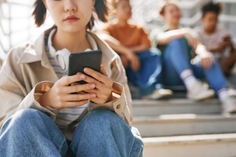 A teen sits alone on a staircase, looking down at a cellphone.