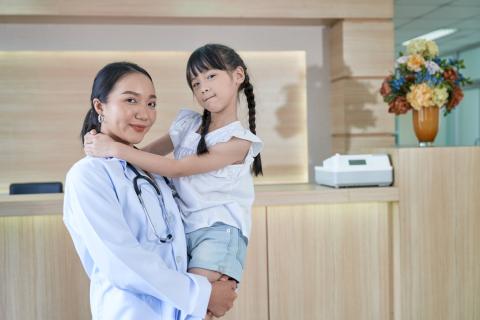 A parent stands in a doctor's office reception area, holding their child