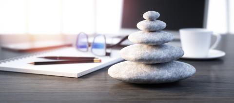 A desk with a computer, paperwork, pens, and a small stack of Zen stones