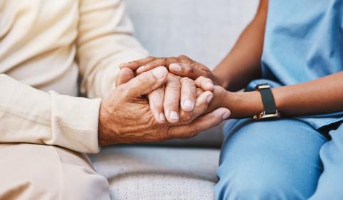 A doctor sits next to a patient, holding their hands.