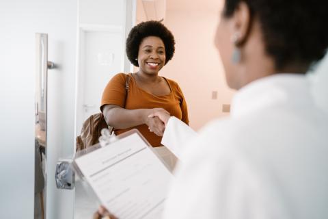 A doctor greets a patient with a smile and a handshake.
