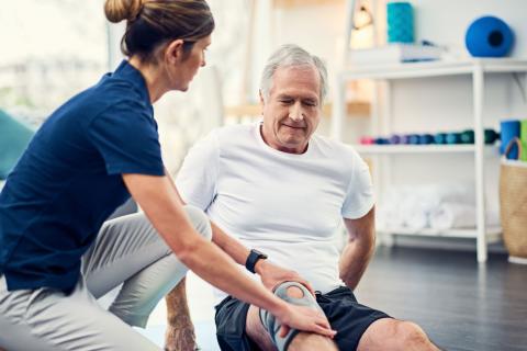 A physiotherapist helps a patient wearing a knee brace extend their leg.