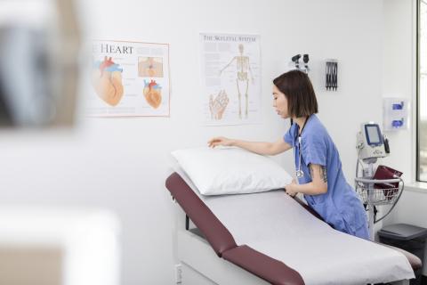A person in scrubs changes the paper on an examination table.