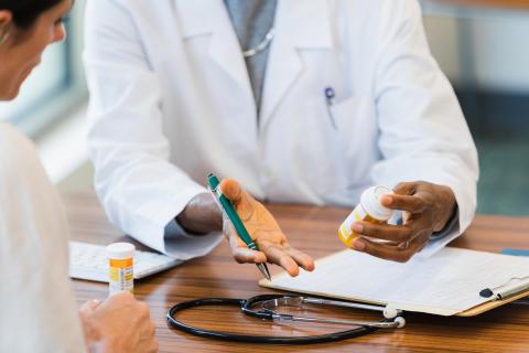 A doctor holds a prescription bottle while talking to a patient.