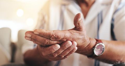 An older person holds one hand in the other, as if in pain.