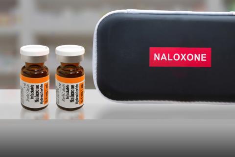 A black rectangular zippered case with the word "Naloxone" beside two brown vials labeled "Injectable naloxone."