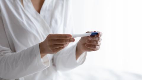 A woman wearing a white shirt or coat looks at a pregnancy test.