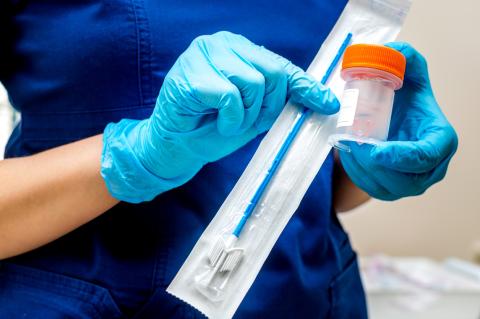 A person wearing scrubs and latex gloves opens a swab kit.