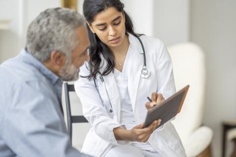 A doctor talks to an older patient, pointing at information on a clipboard.