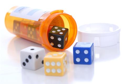 Colorful dice spill out of a prescription pill bottle lying on its side.