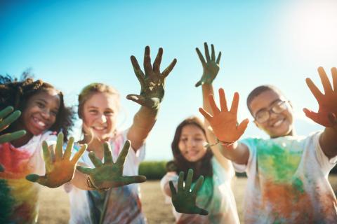 A group of children holding their hands up and facing outward, with paint on their hands and T-shirts.