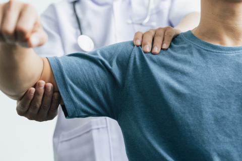 A patient lifts their arm while a doctor tests the range of motion.